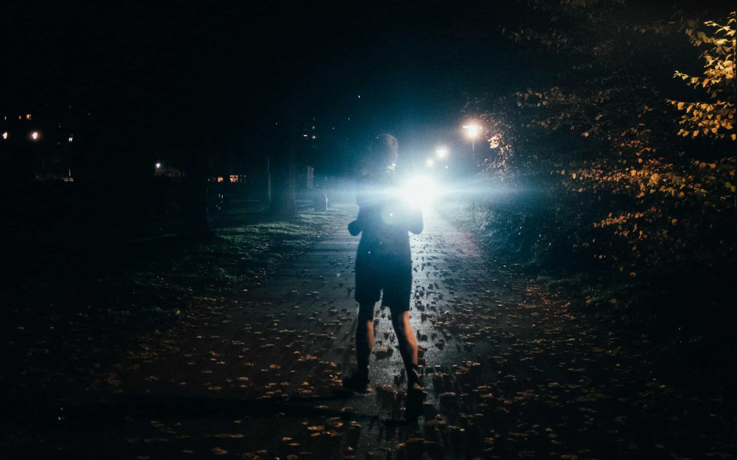 Runner with a bright headlamp on a dark path at night